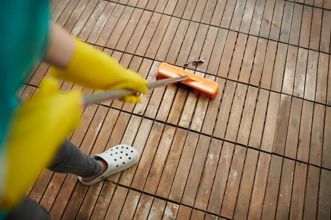 A person sweeping dirt from a composite deck with brush