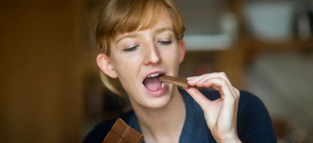 young woman eating chocolate - Does Chocolate Cause Acne? A Complete Guide - Palm Beach Dermatology Group