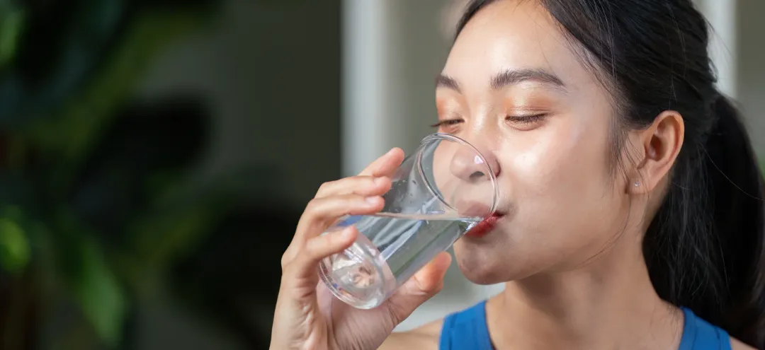 Active woman enjoying a refreshing drink, promoting hydration and wellness in a modern setting. - Does Drinking Water Help With Acne? - Palm Beach Dermatology Gruop